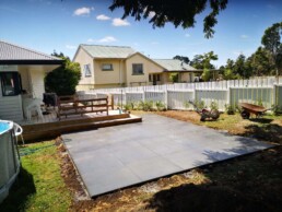 1m Cut Concrete 5kg Black 3 with white fence and yellow house with green roof in the background, and a white house with a deck