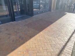pavers on a pedestrian footpath with retail shops in the background, and a man and a family