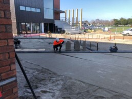 tauranga boys high school paving job with a man measuring the ground and the gymnasium in the background